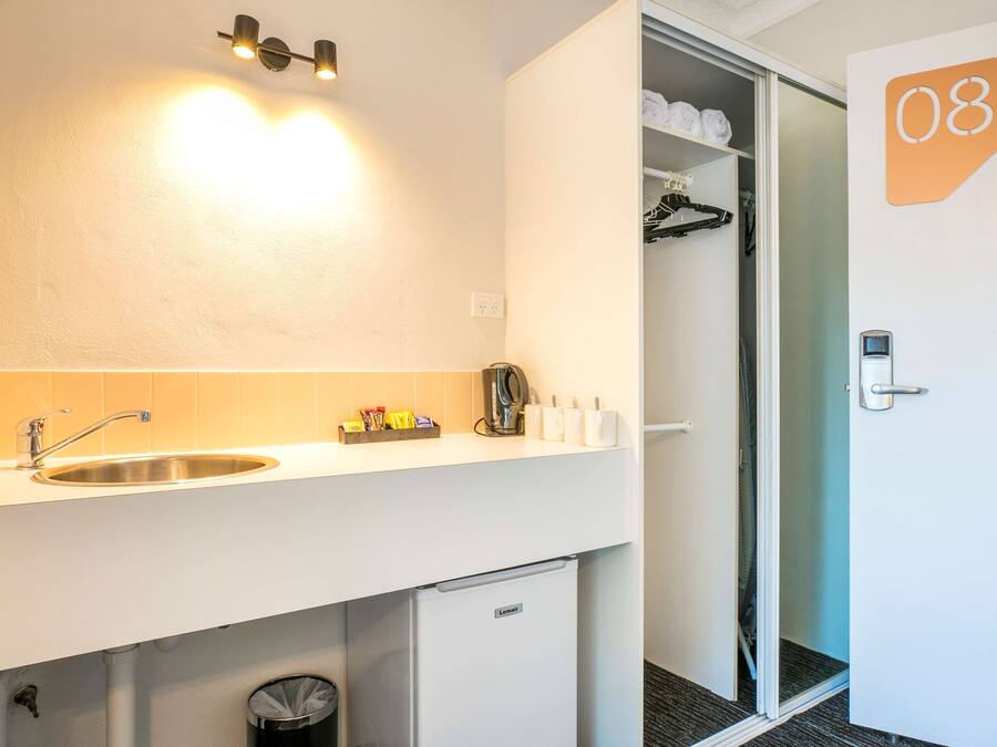 A hotel room with a white sink, a mirror, a small refrigerator, a shower area, and a door marked with the number 08.