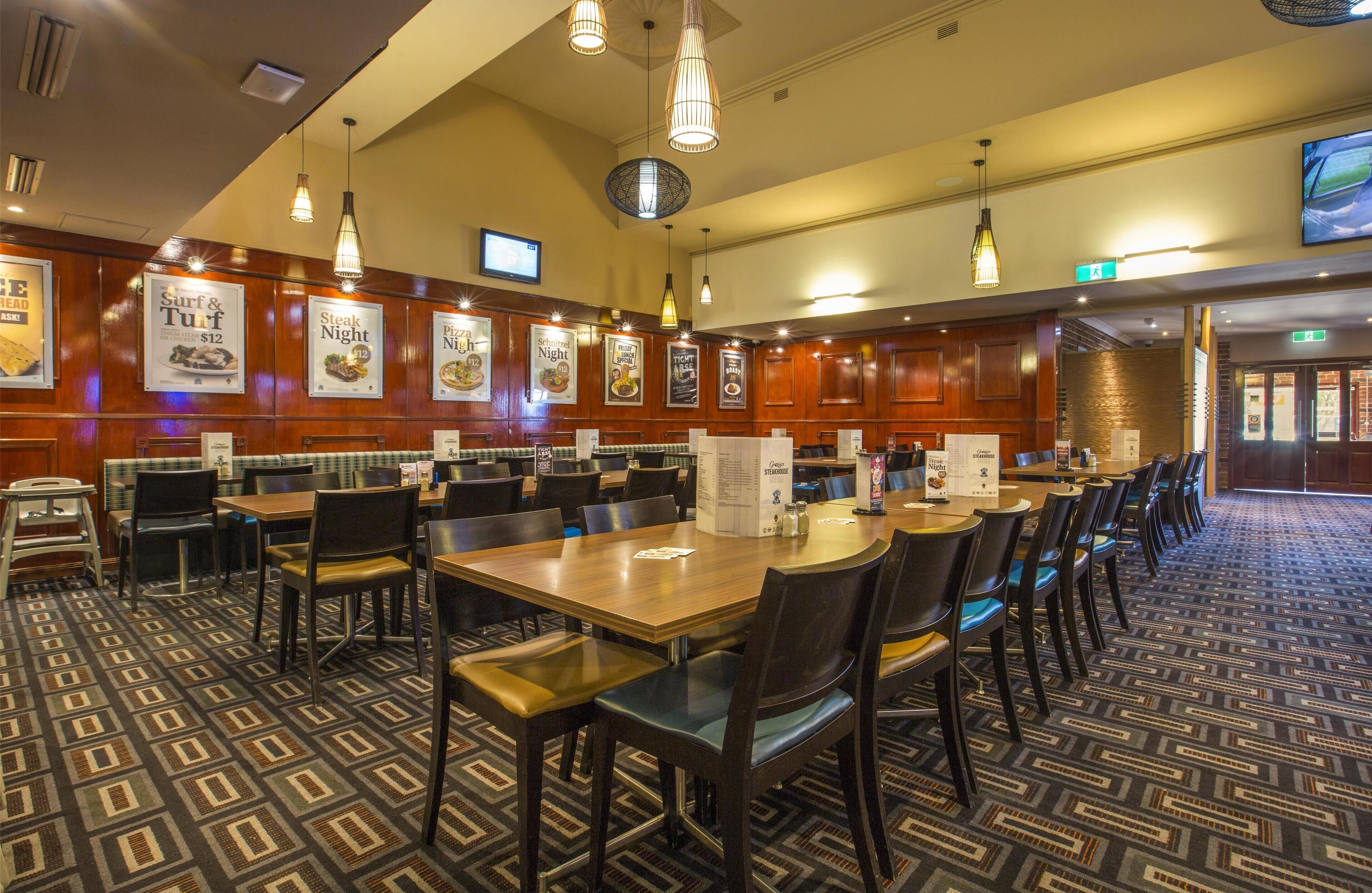 A restaurant with multiple tables and chairs, wooden paneling on the walls, and hanging pendant lights.
