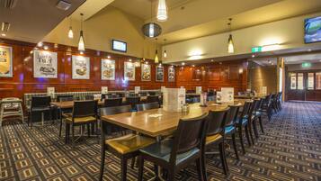 Un ristorante con diversi tavoli e sedie, pannelli in legno sulle pareti e lampade a sospensione.