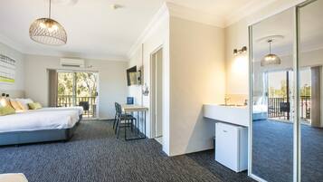 Une chambre d’hôtel équipée d’un lit, d’un bureau et d’une kitchenette. Elle dispose d’une grande fenêtre et d’un balcon.