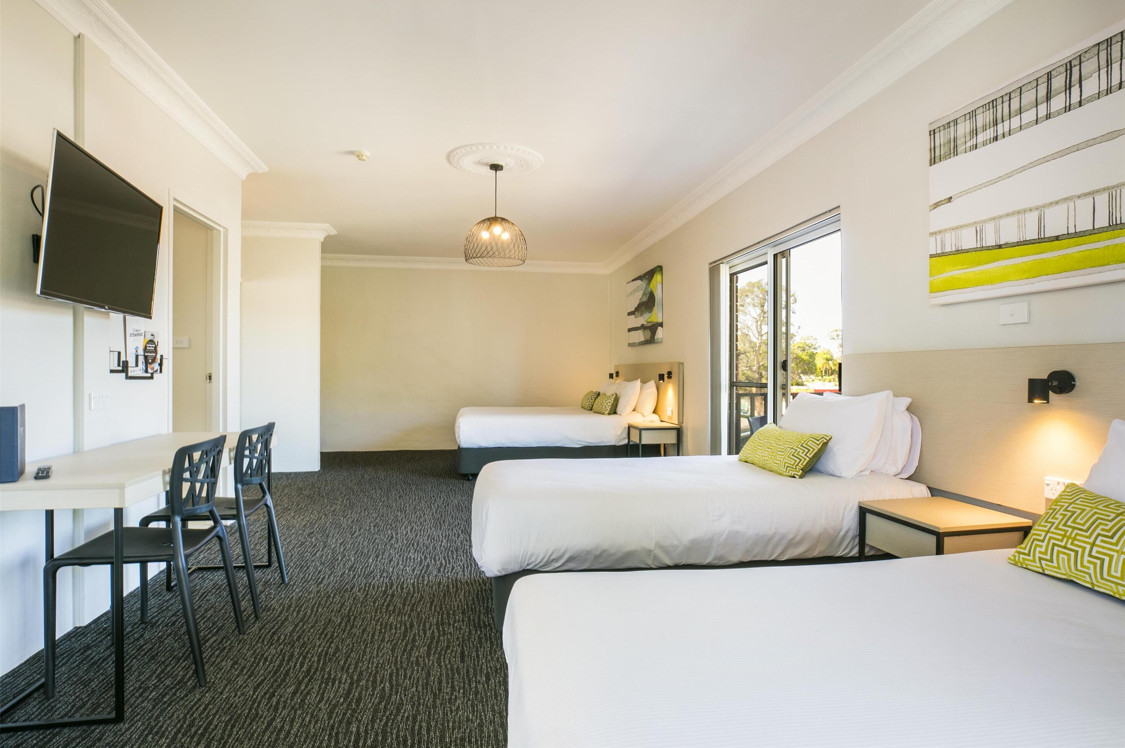 A hotel room with two beds, a desk with chairs, a TV, and a large window.