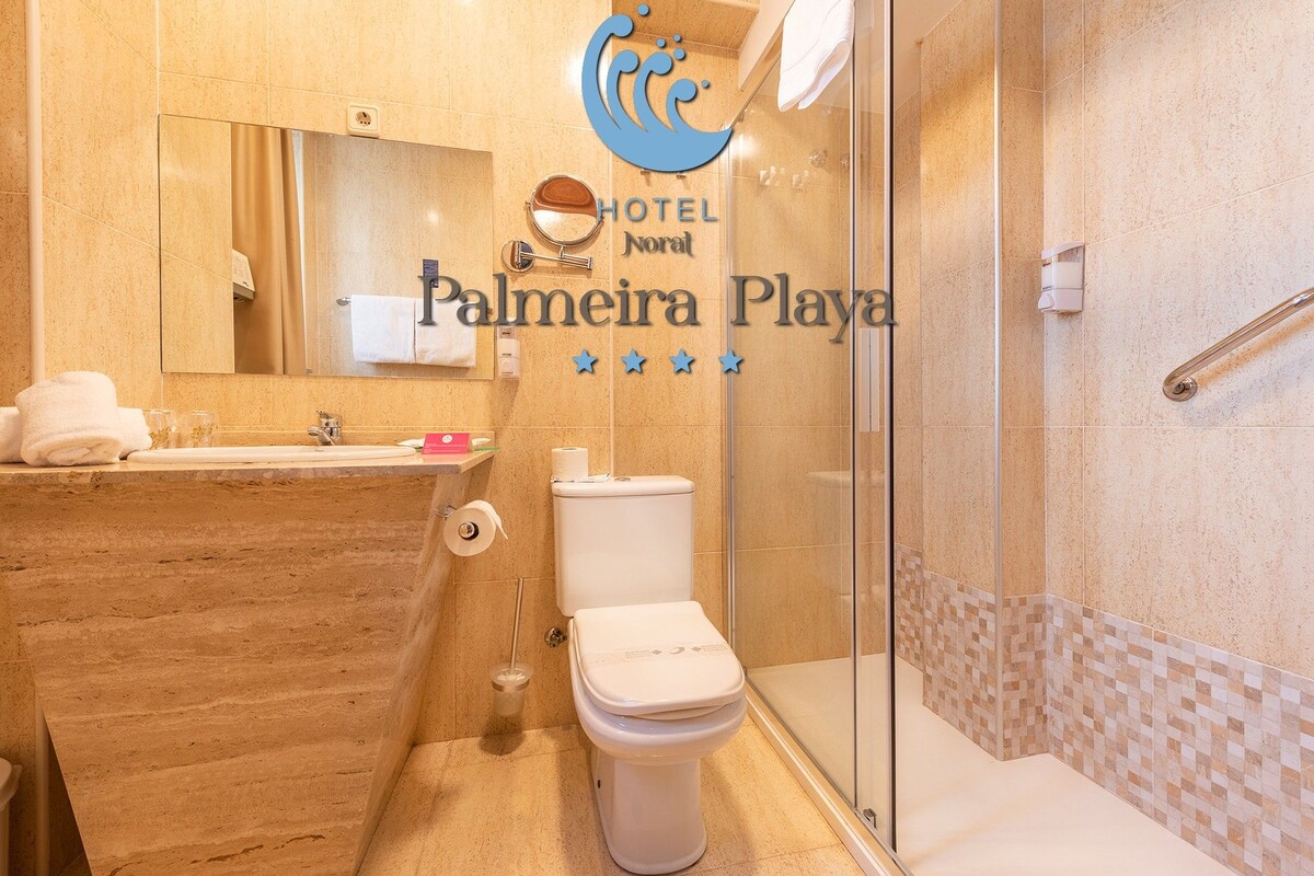 Un baño de hotel con lavamanos, espejo, inodoro y zona de ducha.