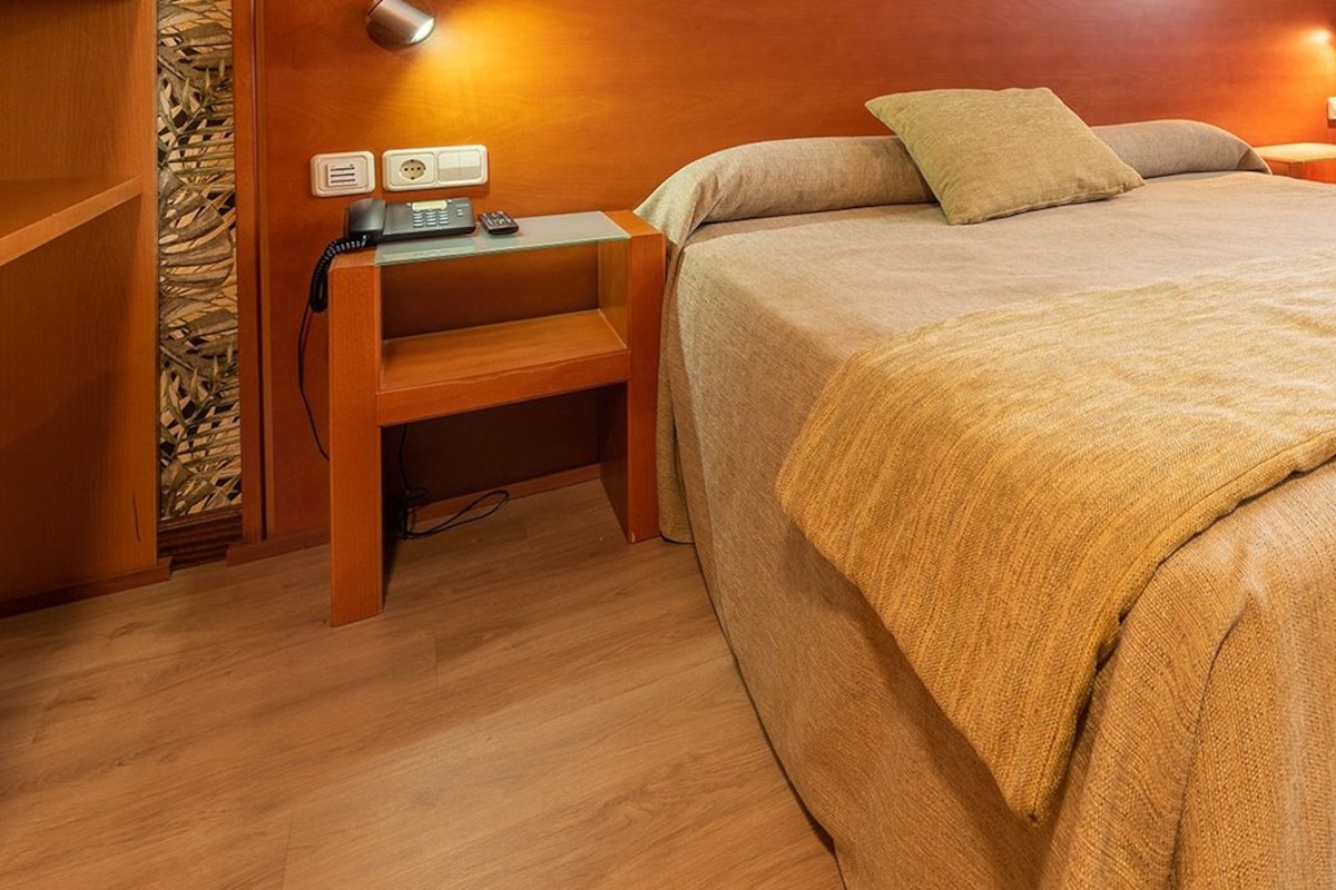 Una habitación de hotel con cama, mesita de noche, silla y escritorio con teléfono.