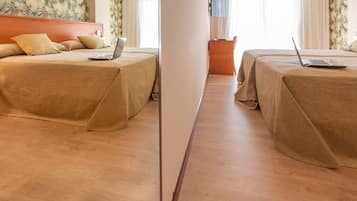 A hotel room with two beds, each with a laptop, wooden flooring, and a small table with a lamp.