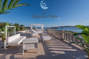 A hotel patio with white furniture, a view of the sea, and a logo for HOTEL Noral Palmaira Playa. - Hotel Norat Palmeira Playa (Ribeira)