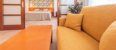 Habitación de hotel con sofá, cama con cabecera, puerta de madera y una planta.