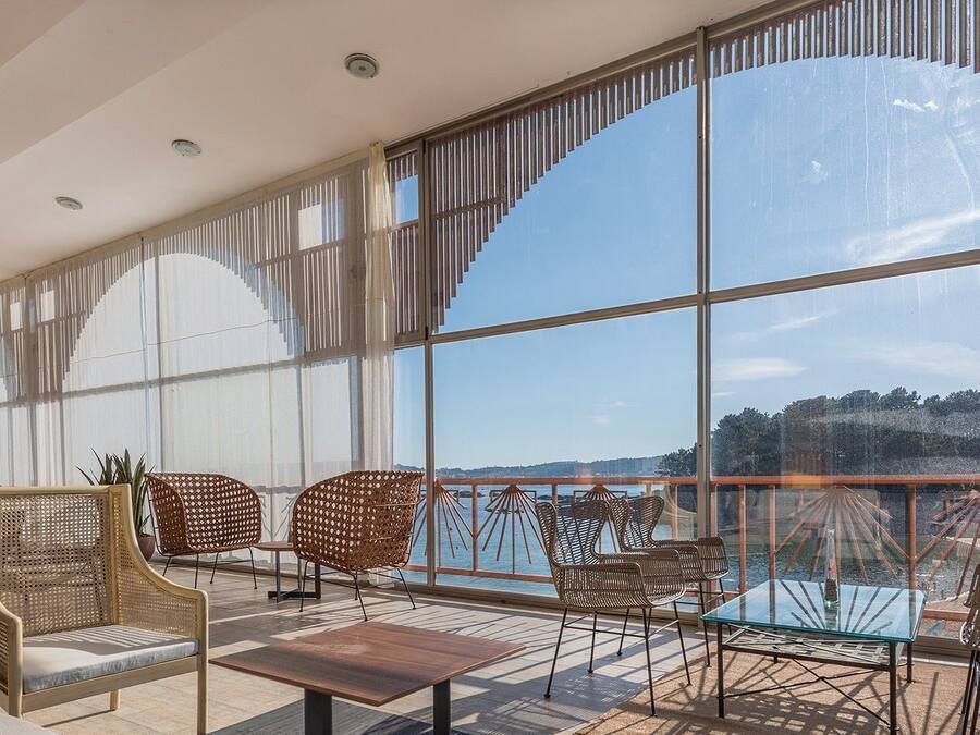 Un balcón amplio con ventanas grandes, mobiliario de mimbre y vista al agua.