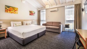 A hotel room with a large bed, a sofa, a desk, and a TV. - Nightcap at the Ranch Hotel (Marsfield)