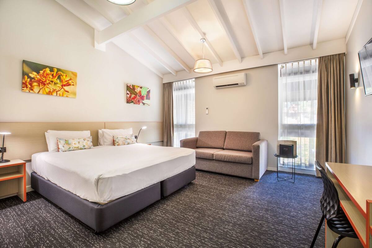 A hotel room with a large bed, a sofa, a desk, and a TV.
