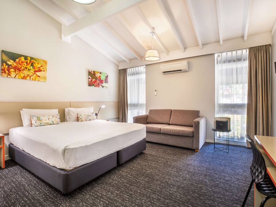 A hotel room with a large bed, a sofa, a desk, and a TV.