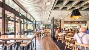 A modern restaurant with wooden tables and chairs, large windows, and a decorative ceiling. - Nightcap at the Ranch Hotel (Marsfield)