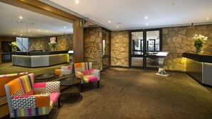 A lobby with a stone wall, a reception desk, colorful chairs, and a large mirror. - Nightcap at the Ranch Hotel (Marsfield)