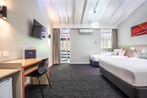 A hotel room with a bed, desk, chair, TV, air conditioning unit, and a view of the outdoors.