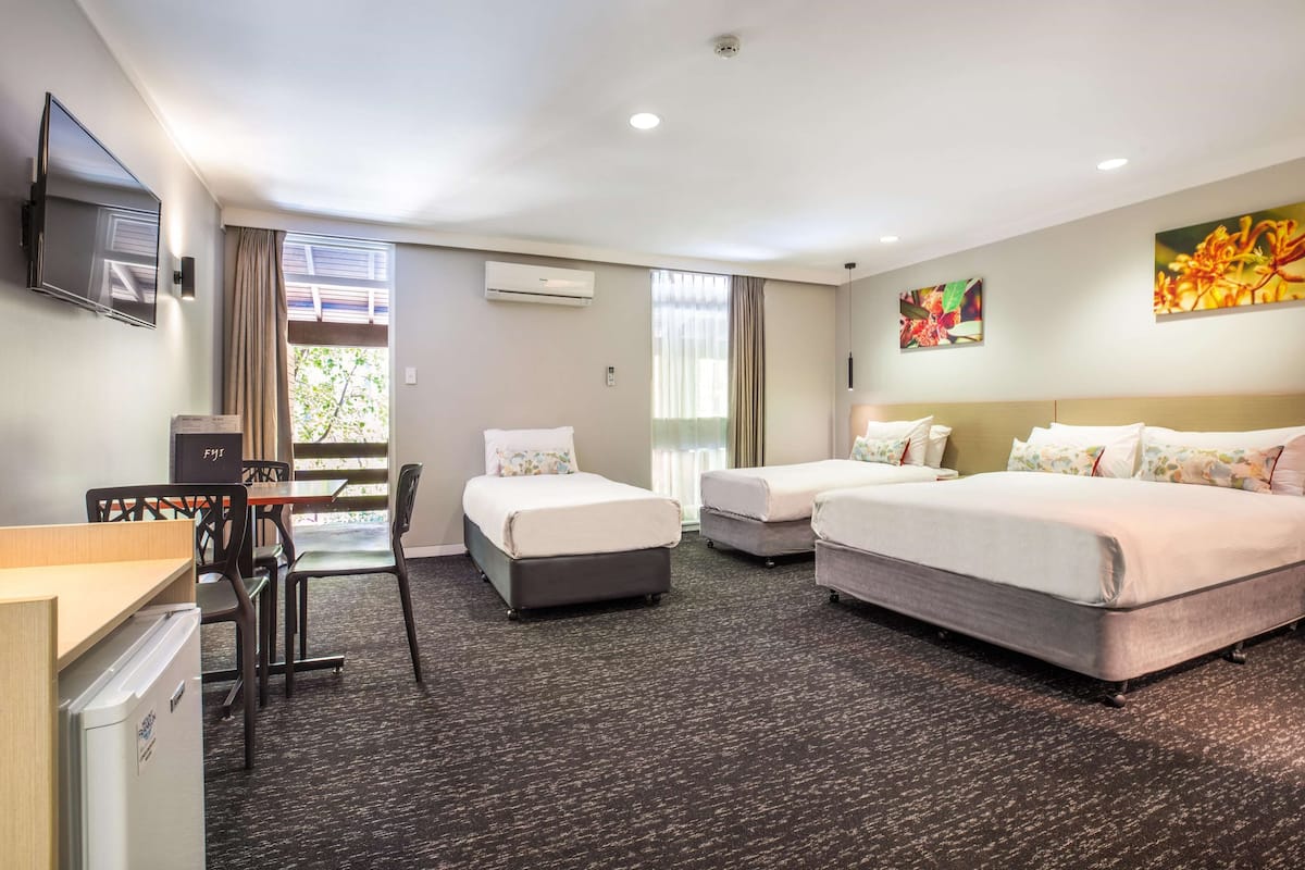 A hotel room with two beds, a desk, and a chair. There is a TV mounted on the wall and an air conditioning unit.