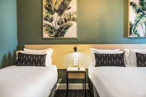 Two single beds with white linens and black patterned pillows, a bedside table with a lamp, and framed botanical prints adorn this stylish room.