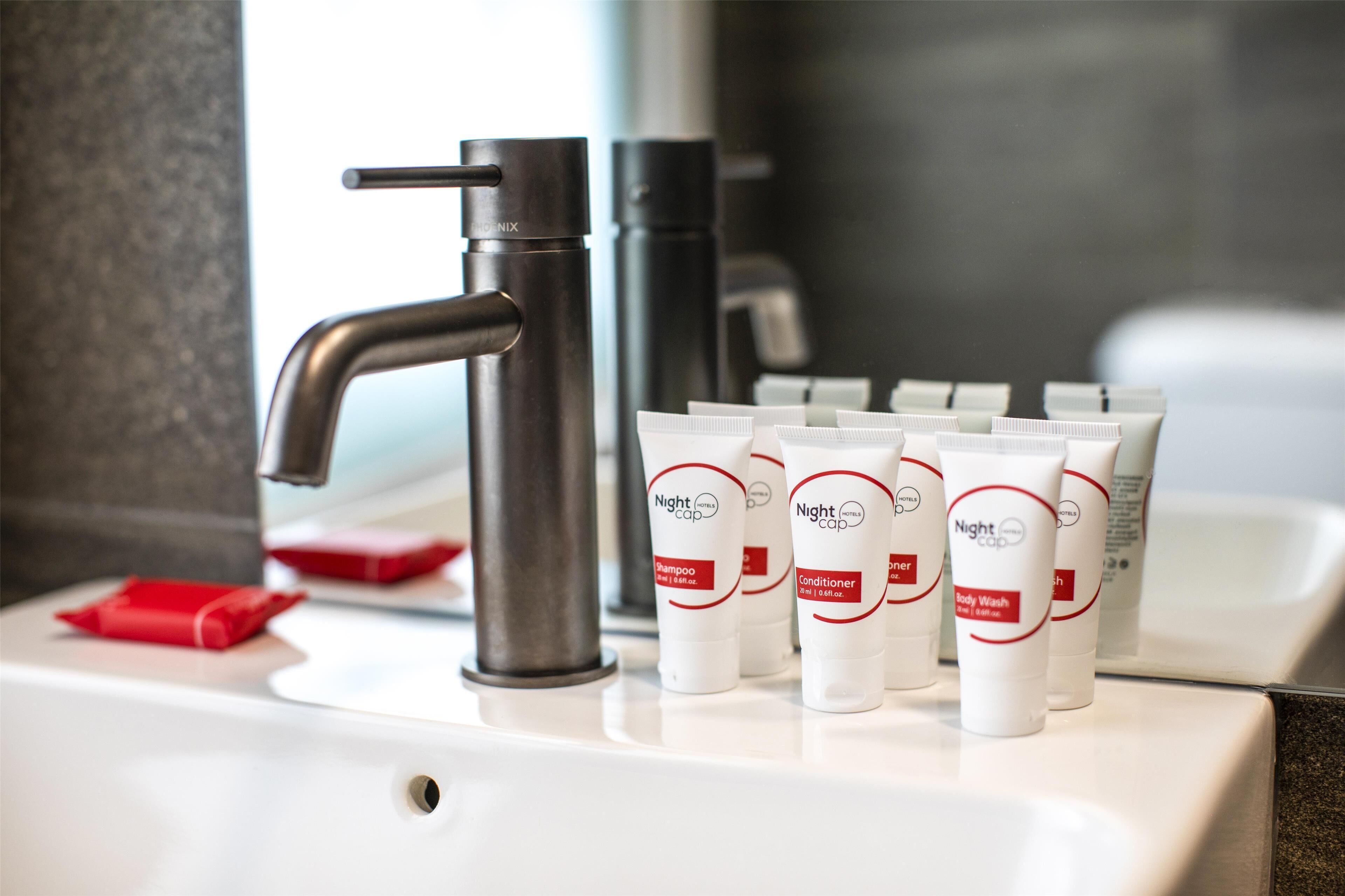 A bathroom sink with a modern faucet, several tubes of Night Cap products, and a red tissue box.
