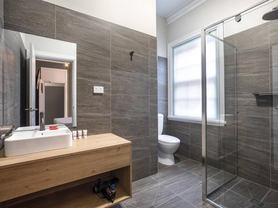 Un baño moderno con tocador de madera, cabina de ducha con mampara de vidrio y inodoro blanco.