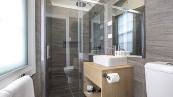 Un baño moderno con ducha de vidrio, tocador de madera con lavabo e inodoro.