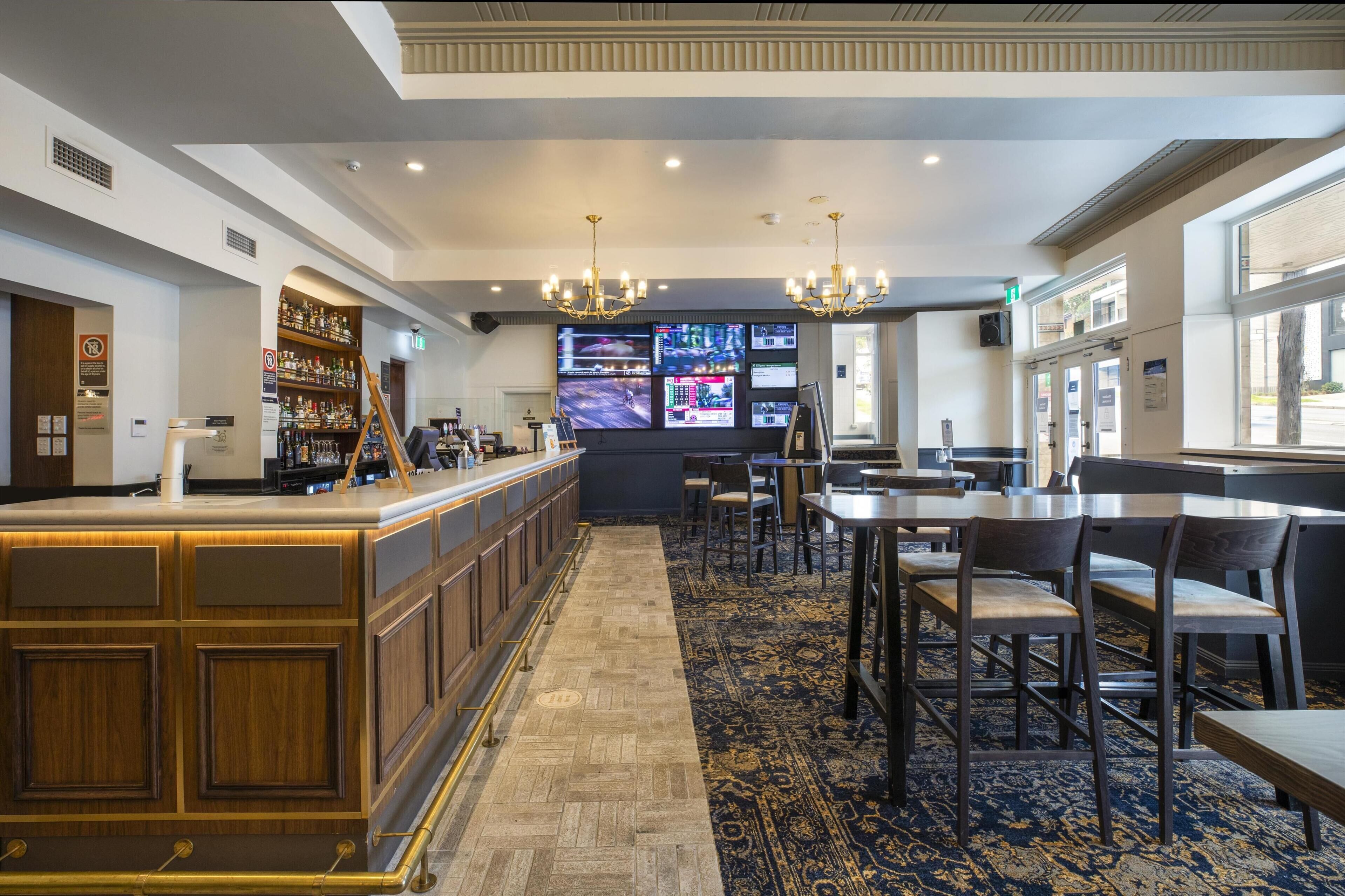 A bar area with a long counter, multiple screens, and seating.