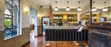 Una zona de bar con mostrador, estanterías llenas de botellas e iluminación colgante.