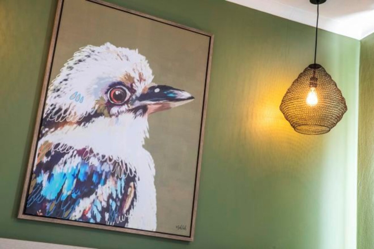 A framed painting of a bird on a green wall, a hanging light fixture, and a ceiling light.