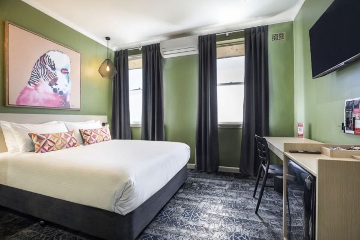A hotel room with a bed, a desk, a chair, a television, and a window with curtains.