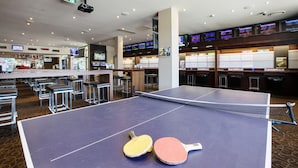 A ping pong table with two paddles in a hotel lobby with multiple screens and bar seating. - Nightcap at Pritchards Hotel (Mt Pritchard)