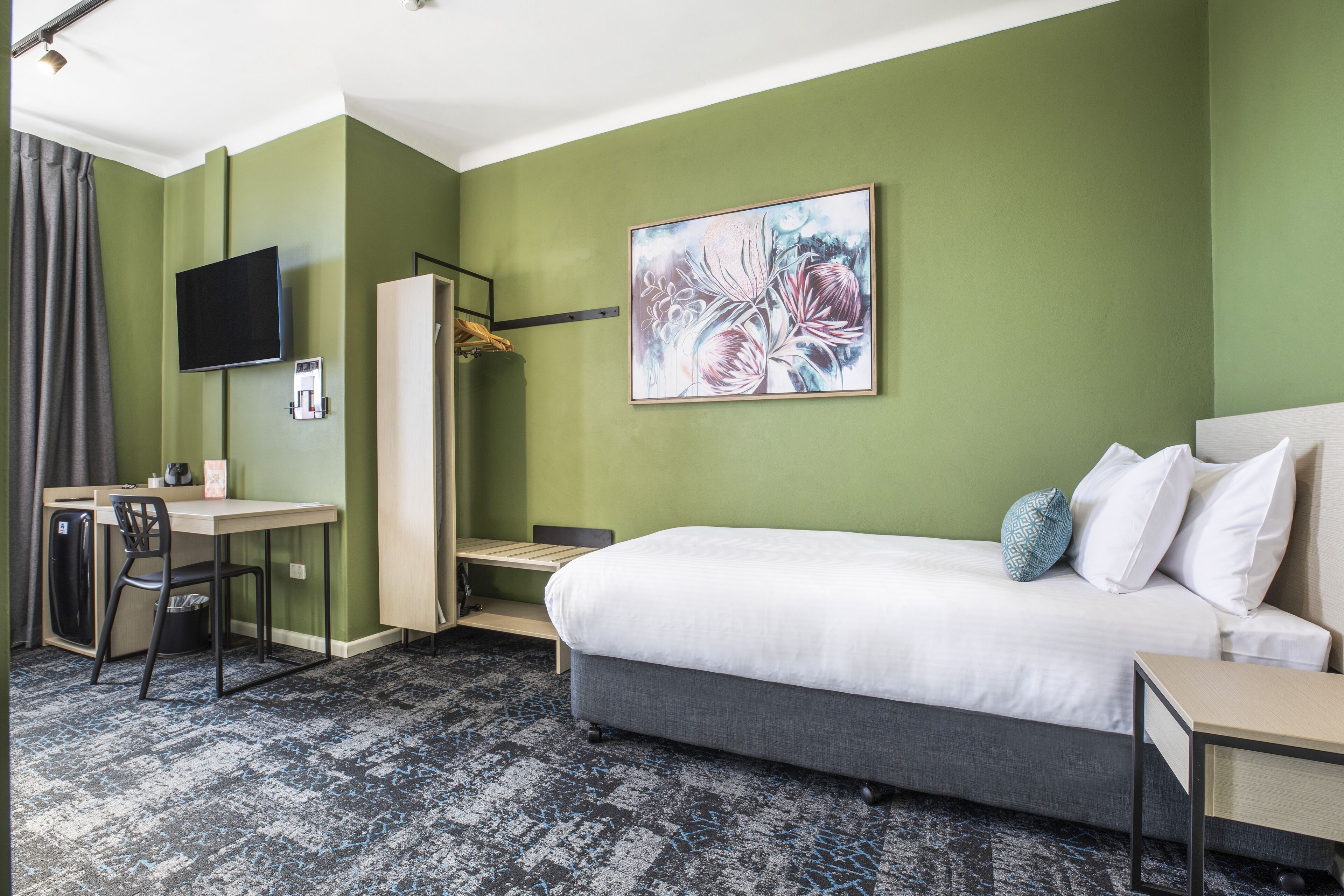 Habitación de hotel con cama, escritorio, silla, televisor y un cuadro en la pared.