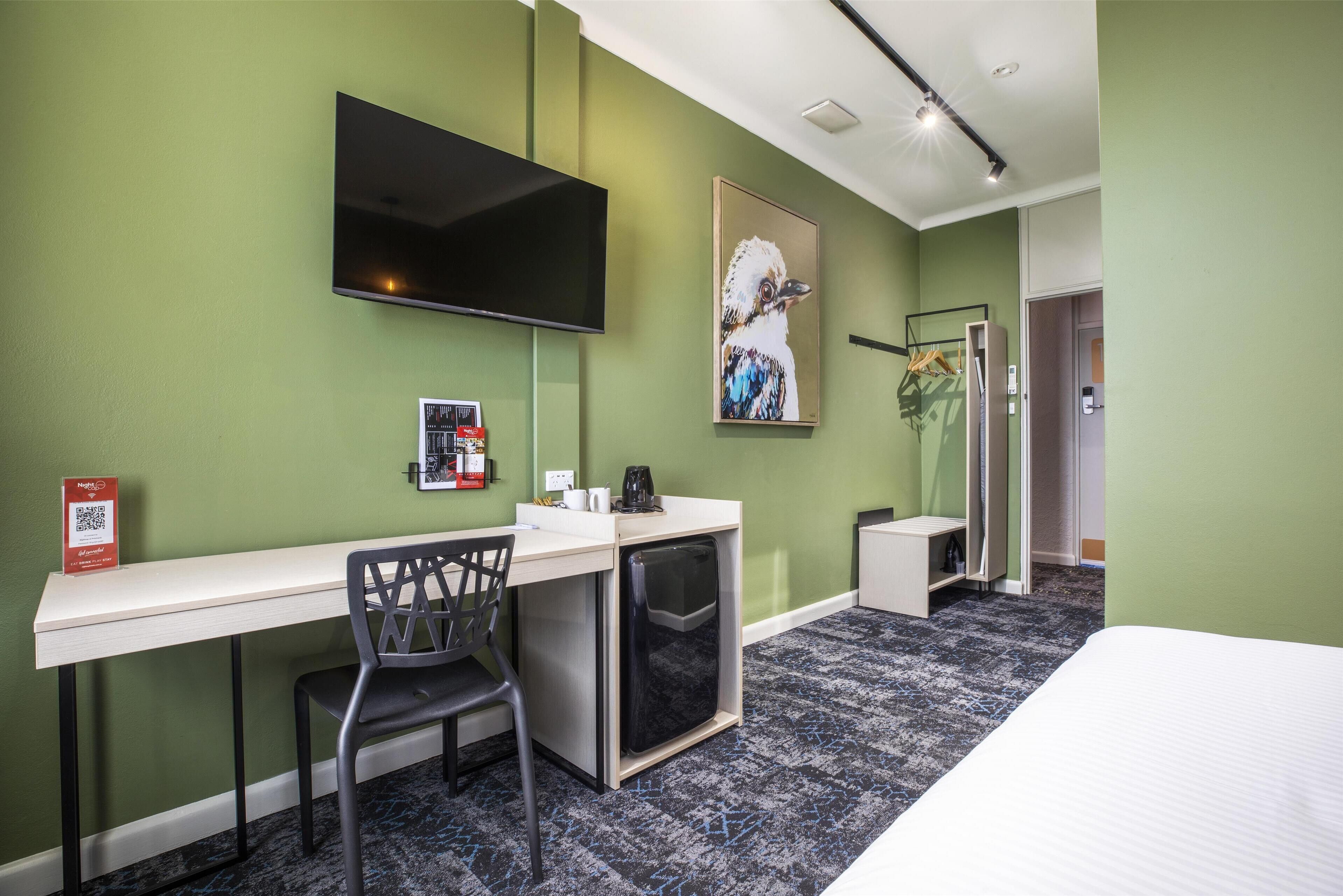 Una habitación de hotel con escritorio, silla, cama y televisor montado.