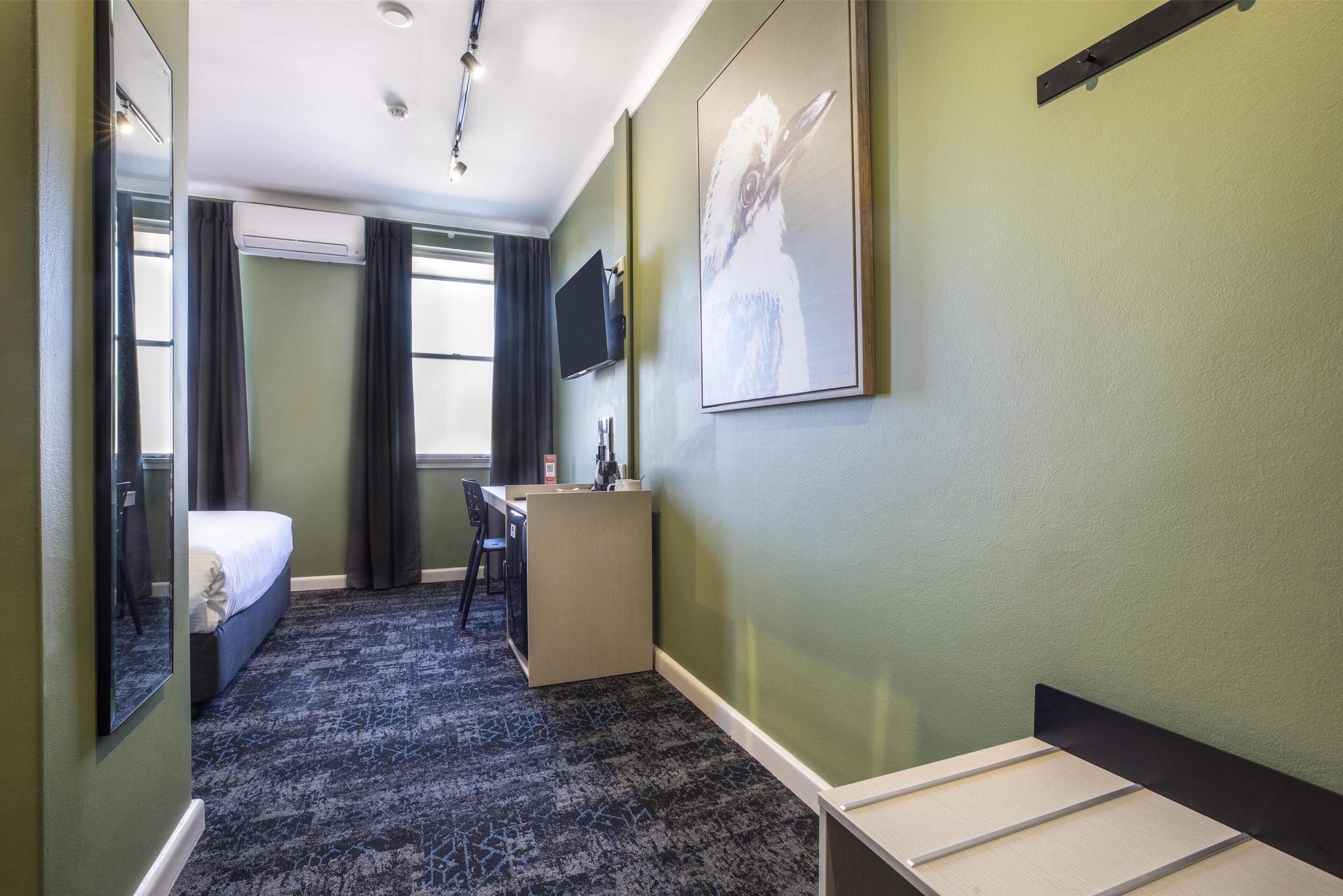 A hotel room with a bed, desk, and a mounted TV.