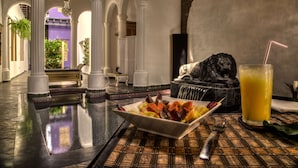 A dining area with a table set for two, featuring a fruit platter and a glass of orange juice. - Casa de Leda, a Kali Hotel (Santa Marta)