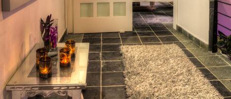 Un pasillo con una mesa de vidrio que sostiene velas, una alfombra y un cuadro en la pared.