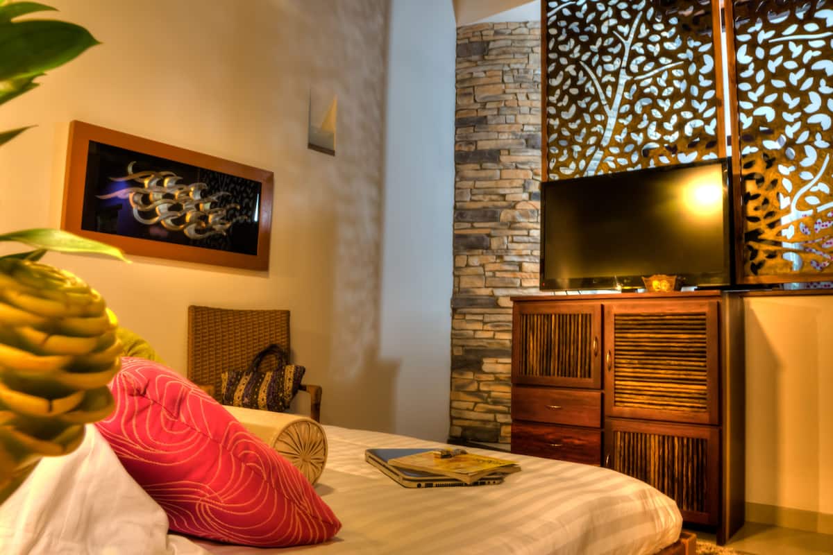 A hotel room with a bed, a television, a decorative wall panel, and a plant.
