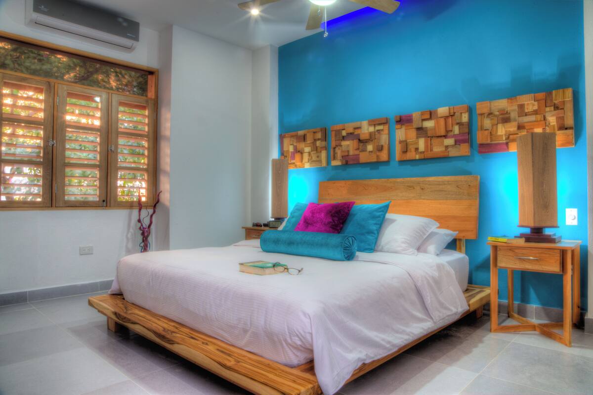 A bedroom with a wooden bed, a nightstand, a lamp, and a wall with wooden art pieces.