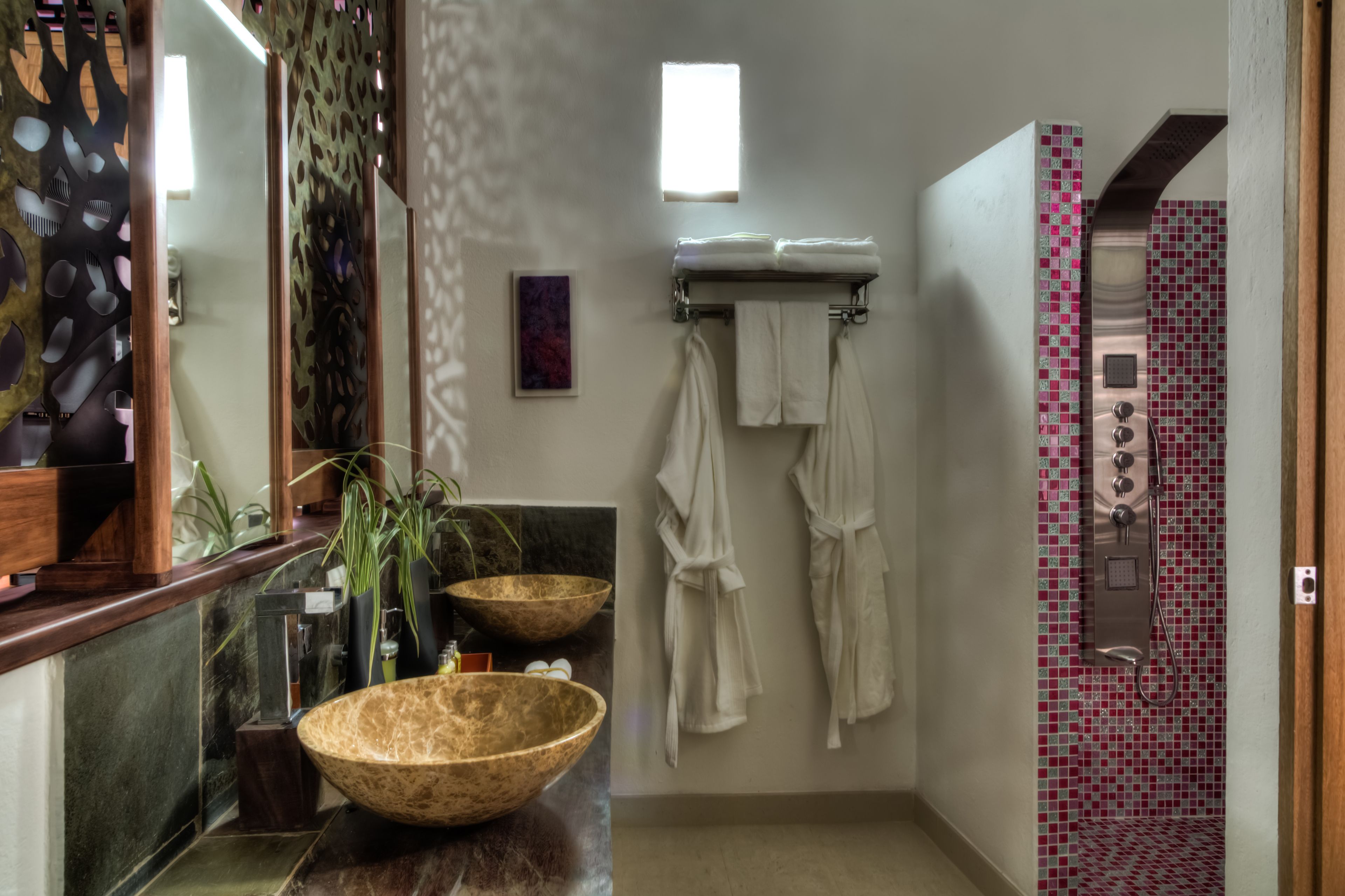 A bathroom with a large wooden bowl sink, a mirror, two white towels, and a shower with pink mosaic tiles.