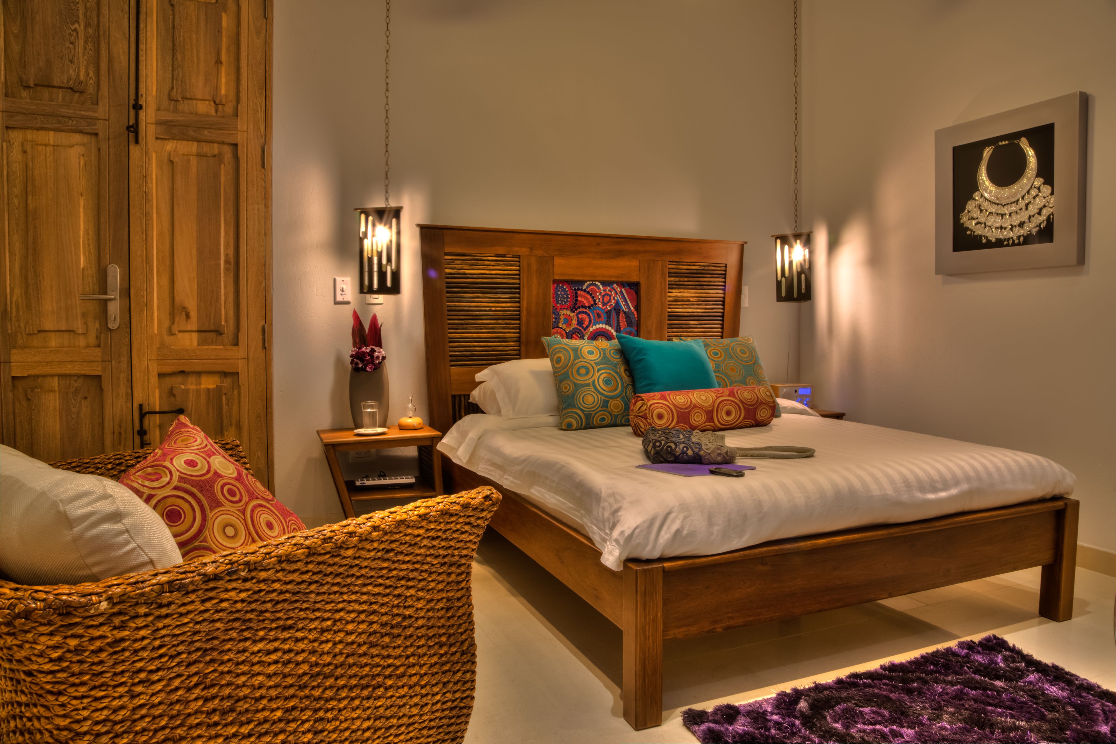 A bedroom with a wooden bed, colorful pillows, a woven chair, and a purple rug.