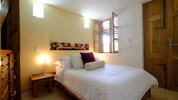 A bedroom with a bed, bedside table, lamp, artwork on the wall, and a wooden wardrobe.