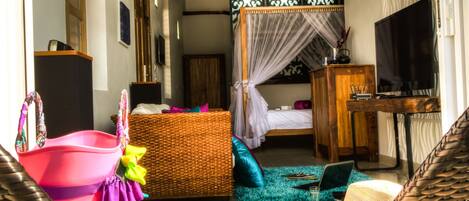 A room with wicker furniture, a bed with a canopy, a television, and a desk.