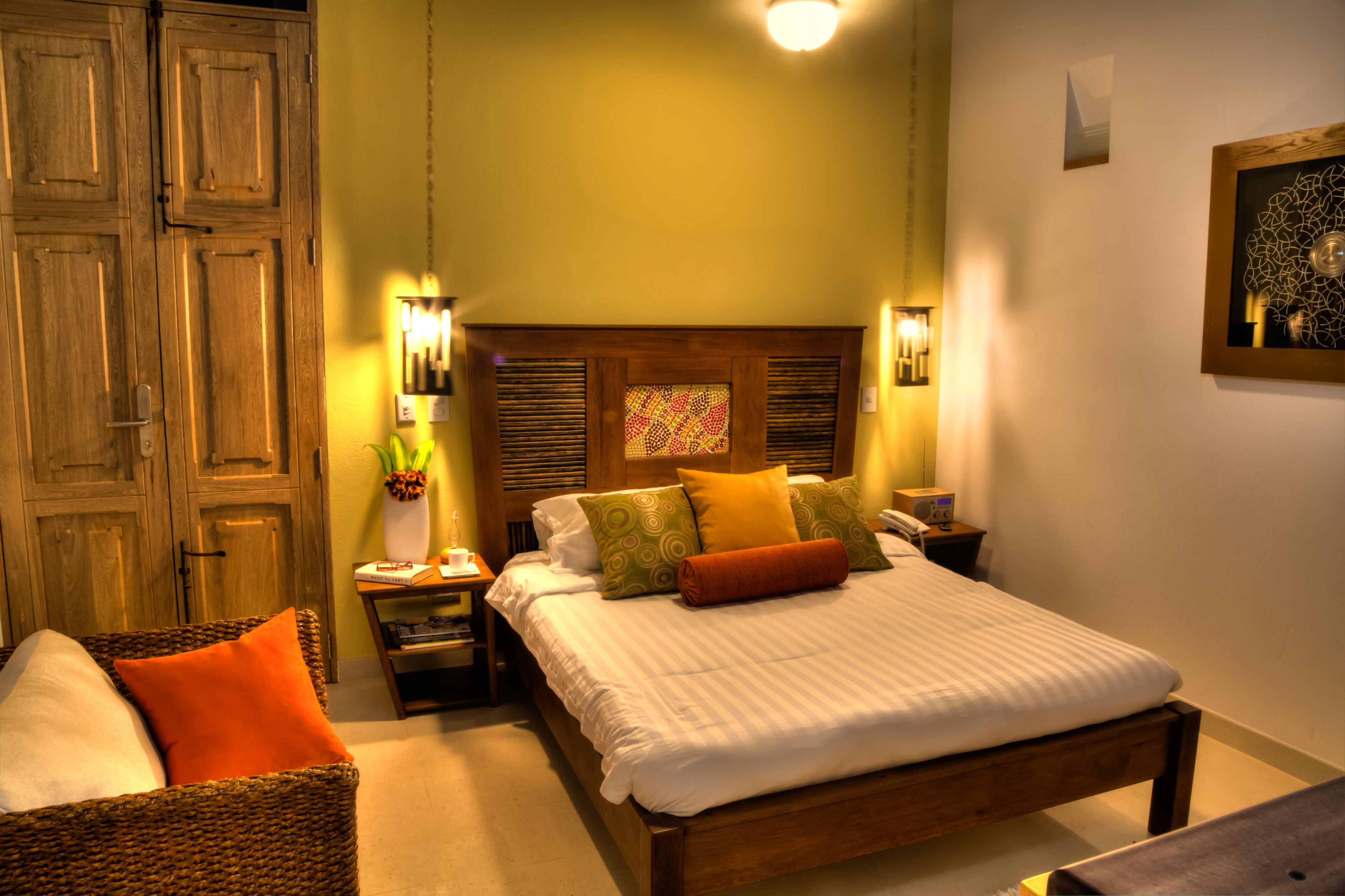 A neatly arranged bedroom with a wooden bed, a wicker chair, and a nightstand with a lamp.