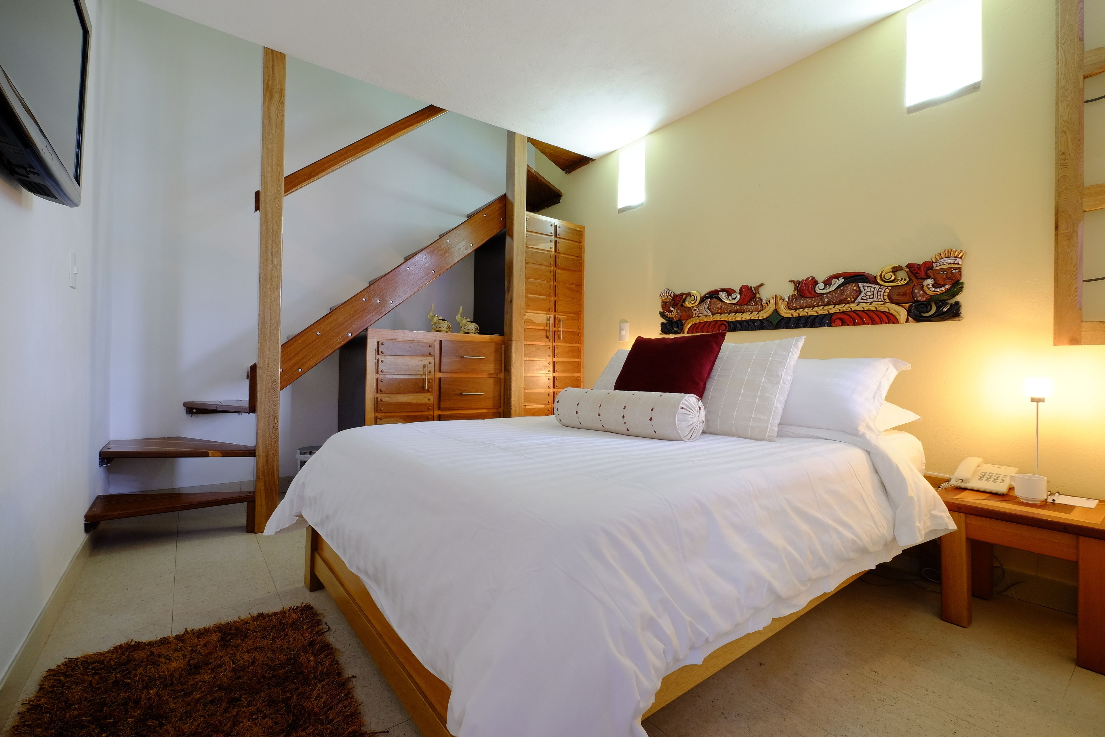 Un dormitorio con una cama de madera, un escritorio pequeño con una lámpara, un teléfono en la pared y una escalera.