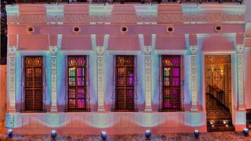 Fachada de edificio con columnas ornamentales, molduras decorativas y una serie de ventanas con rejas de metal.