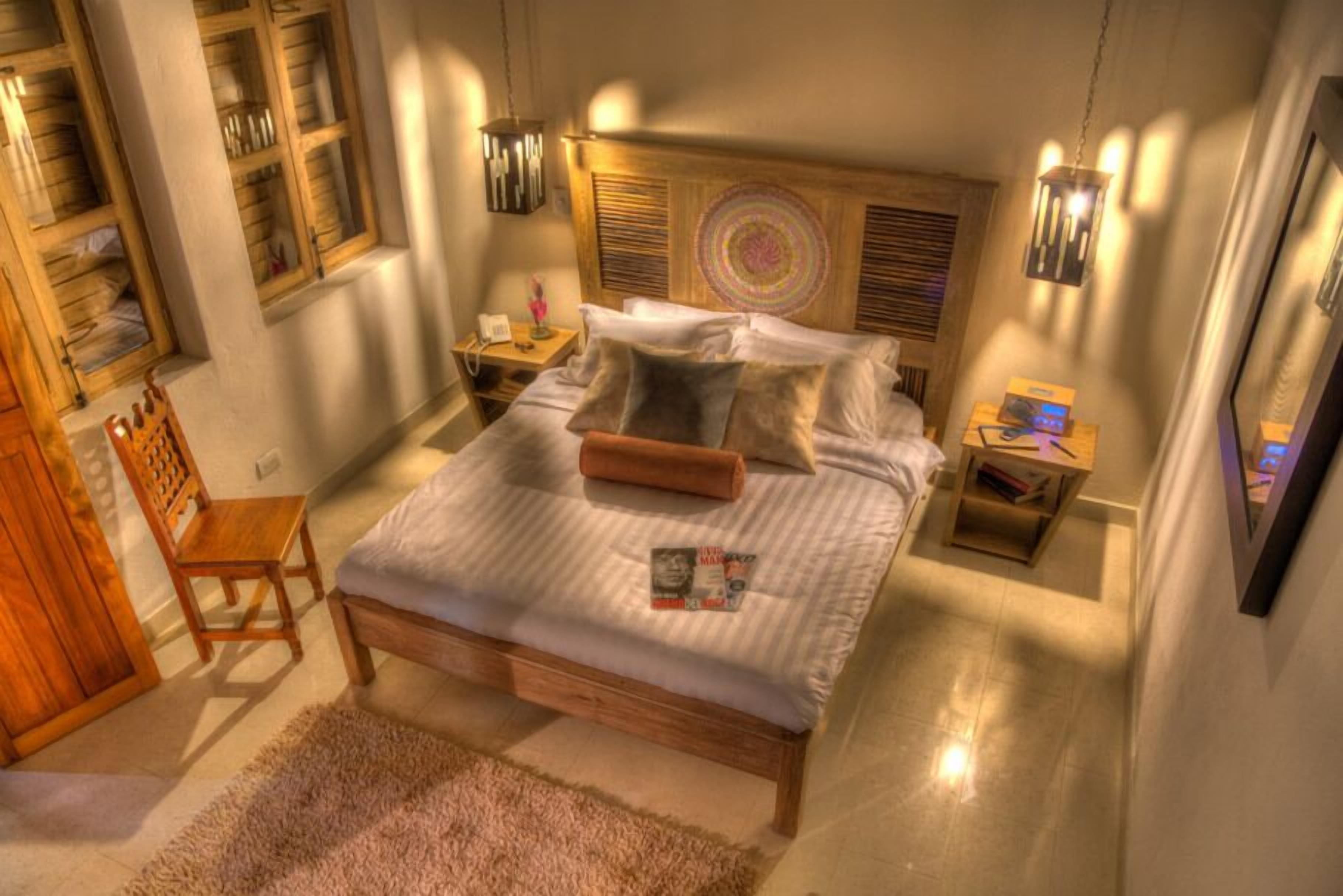 Un dormitorio ordenado con una cama de madera, una mesita de noche, una silla y una pequeña mesa con una lámpara.