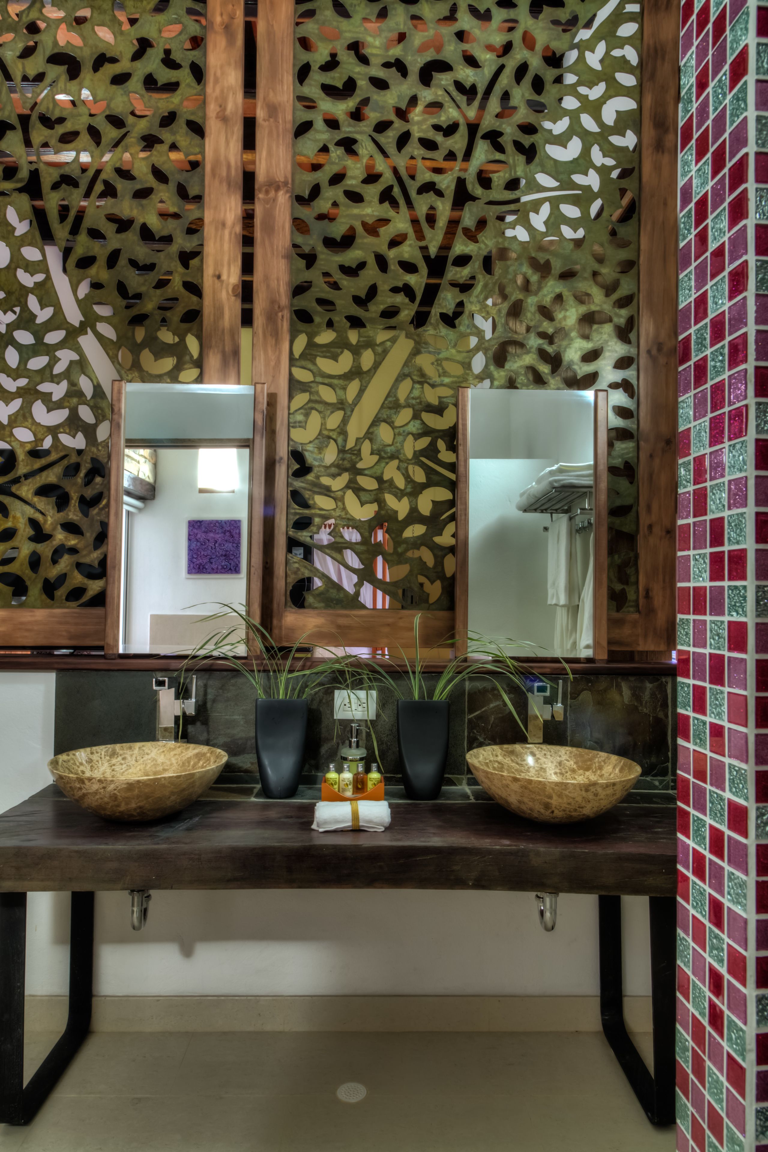 Casa de banho com toucador de madeira, duas espelhos grandes e um painel decorativo com padrões de folhas.