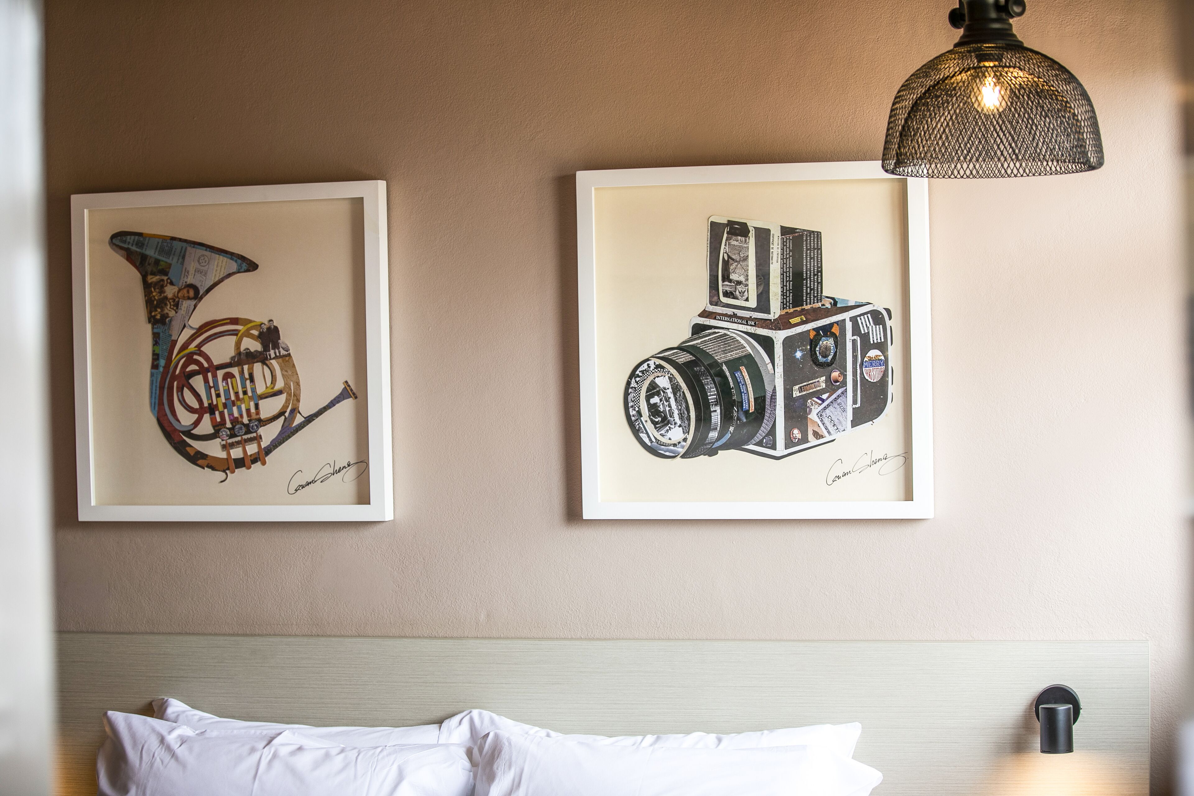 Two framed artworks on a wall above a bed with a headboard.