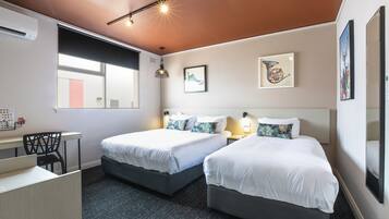 Habitación de hotel con dos camas, un escritorio y una silla. Cuenta con luces fijadas en la pared y obras de arte.