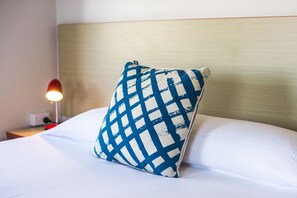 Un lit bien fait, avec un oreiller à carreaux bleus et blancs et un oreiller blanc.