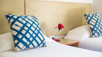 A hotel room with two beds, each with a checkered pillow, a red lamp, and a wooden headboard.