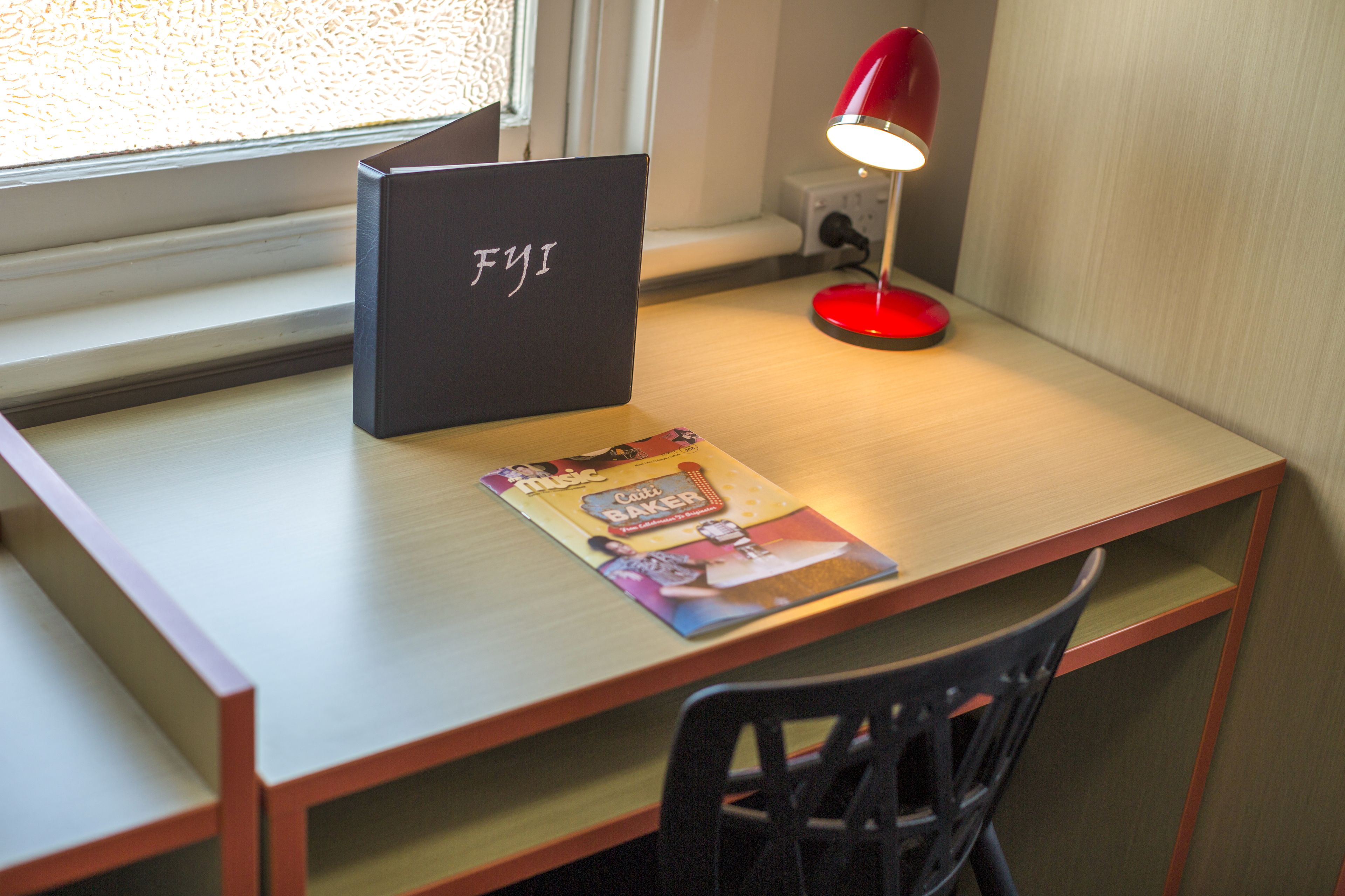 A desk with a laptop, a red desk lamp, and a magazine.