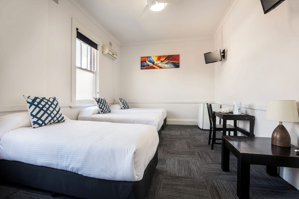 A hotel room with two beds, a desk, a chair, a TV, and a painting on the wall.