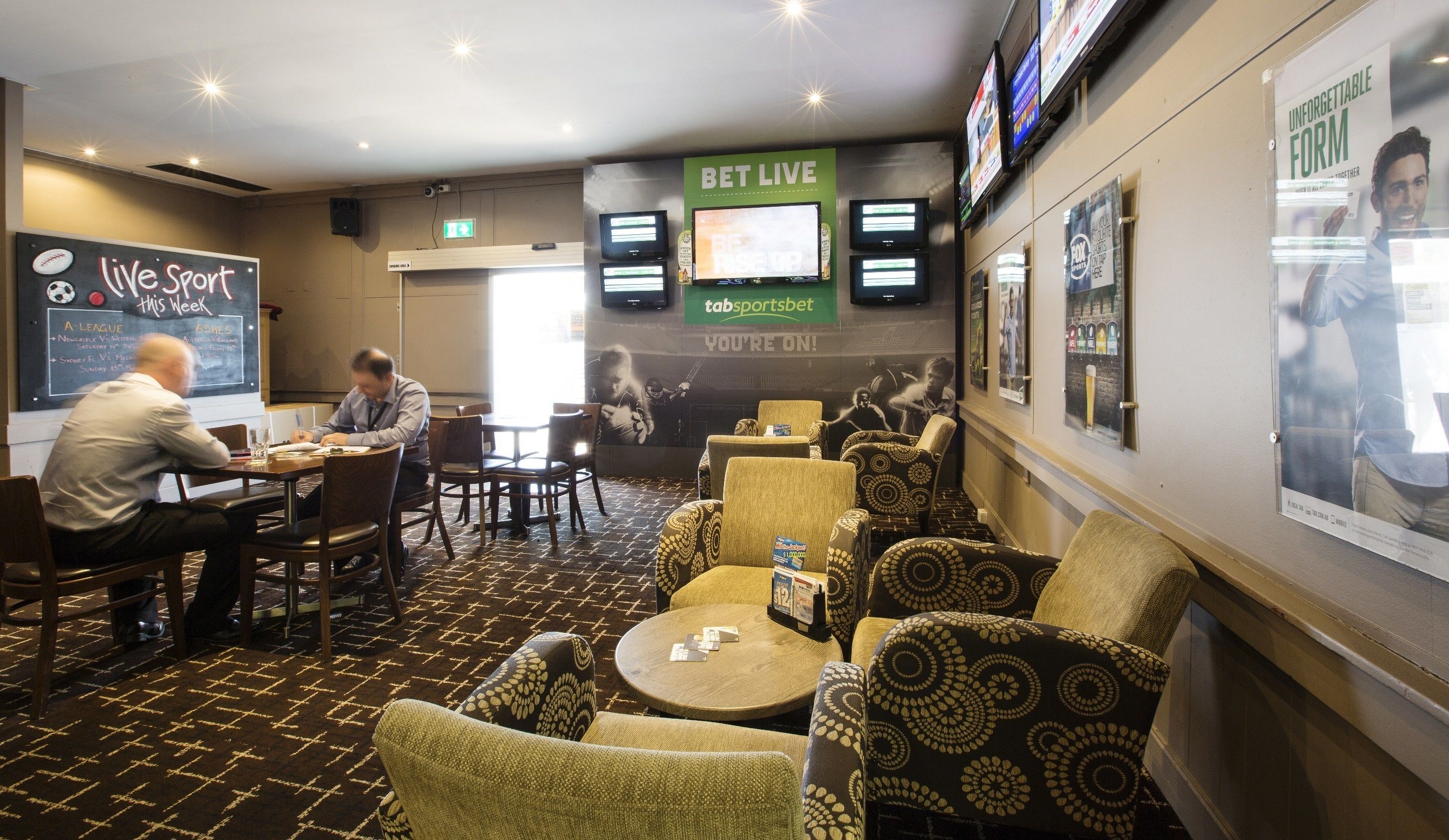 A hotel lobby with a sports betting area, including a large screen displaying sports events, multiple betting tables, and comfortable seating.